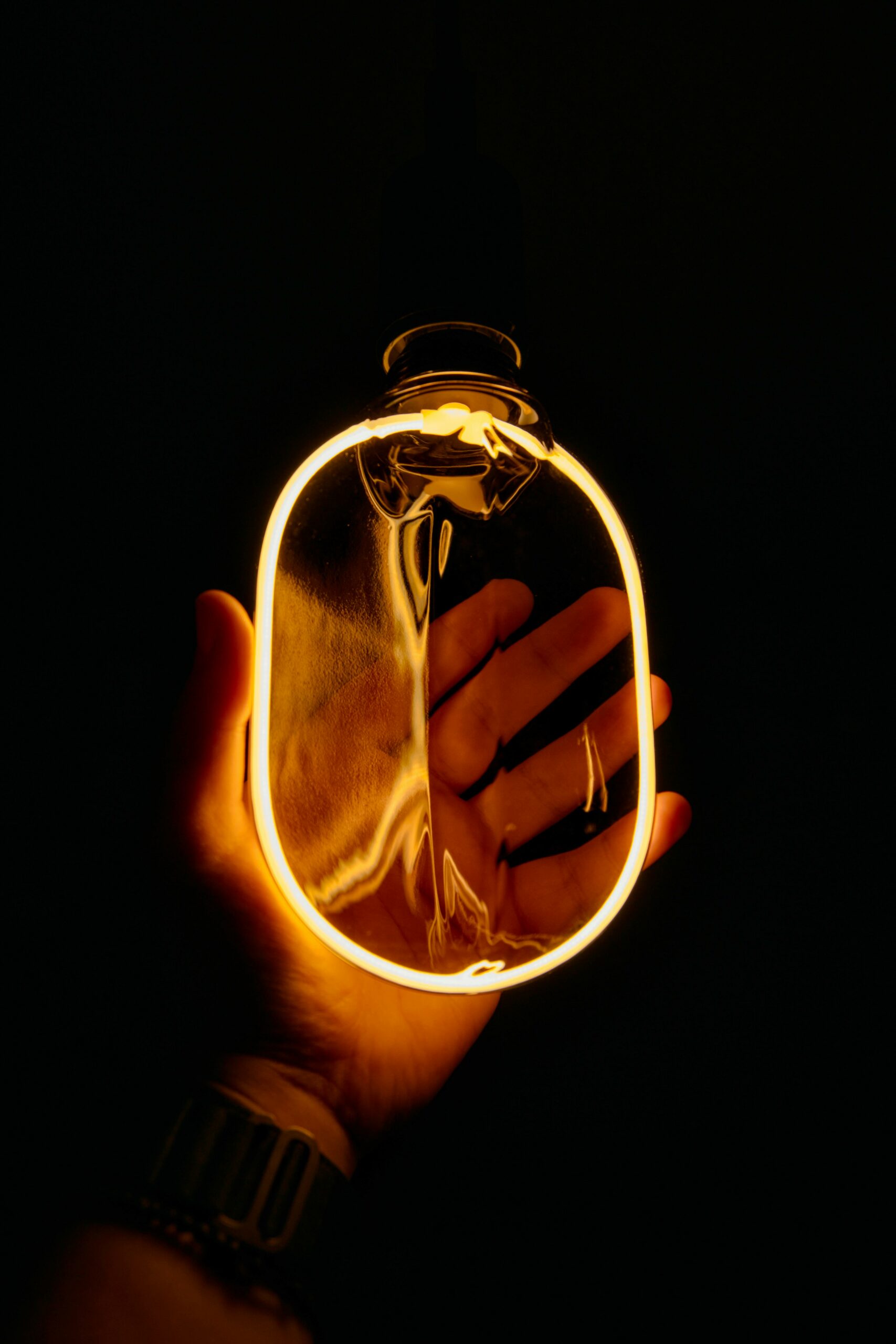 A hand holding a glowing filament bulb creates a cozy and warm ambiance against a dark background.